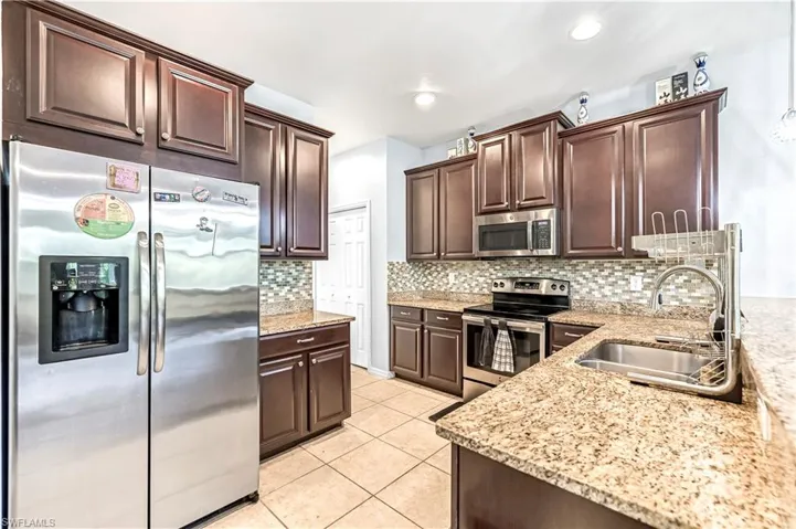 Kitchen featuring appliances with stainless steel finishes, dark brown cabinetry, light stone counters, light tile patterned floors, and decorative backsplash