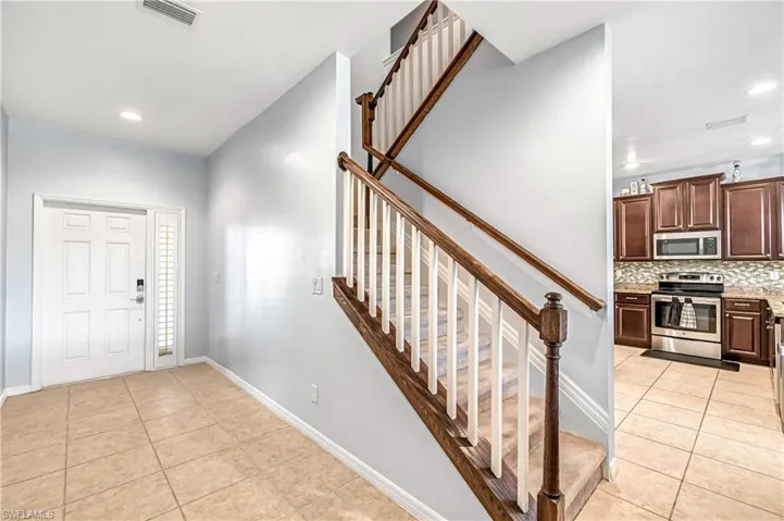 Foyer entrance with light tile patterned floors, recessed lighting, and stairway