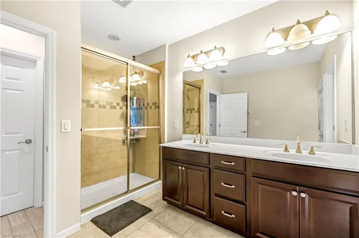Bathroom featuring a stall shower, double vanity, and light tile patterned floors