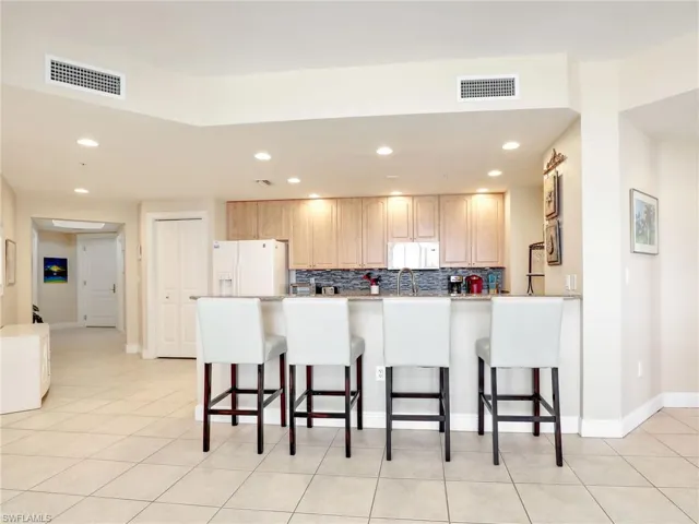 Kitchen featuring a breakfast bar area, light tile floors, white appliances, and backsplash