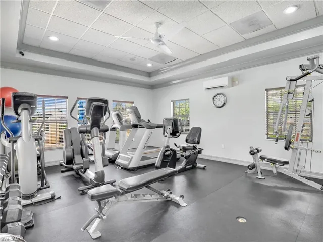 Exercise room with an AC wall unit, ceiling fan, a wealth of natural light, and a paneled ceiling