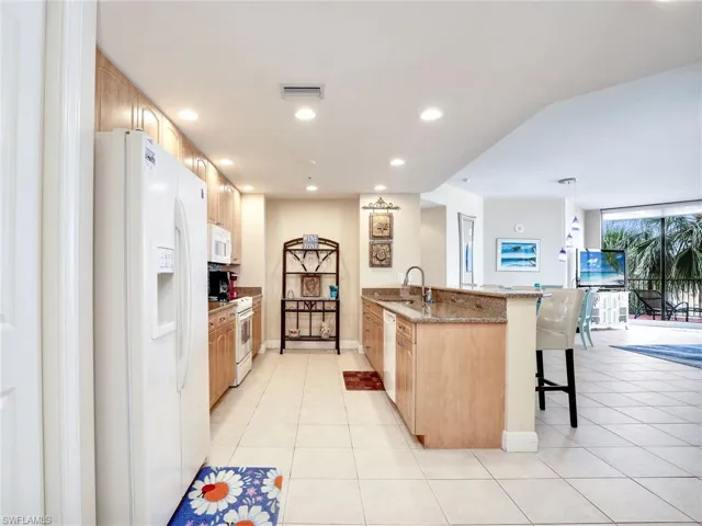 Kitchen with kitchen peninsula, white appliances, light stone counters, light tile floors, and a breakfast bar area