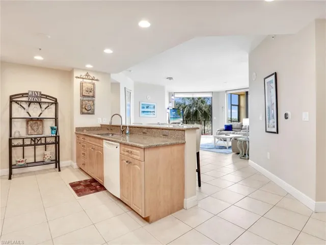 Kitchen featuring light stone countertops, kitchen peninsula, white dishwasher, sink, and a breakfast bar