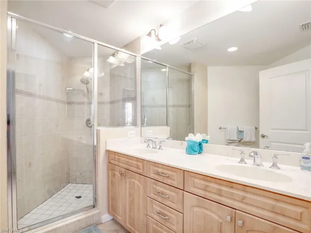 Bathroom featuring a shower with shower door, tile flooring, oversized vanity, and dual sinks