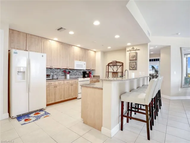 Kitchen featuring light stone countertops, tasteful backsplash, light tile flooring, and white appliances