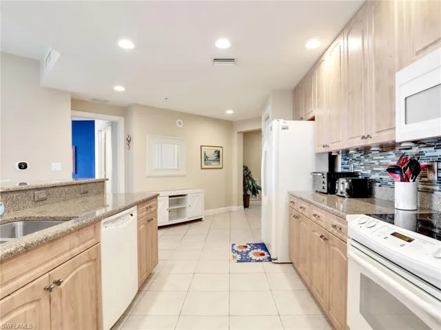 Kitchen featuring light brown cabinets, white appliances, light stone counters, backsplash, and light tile floors