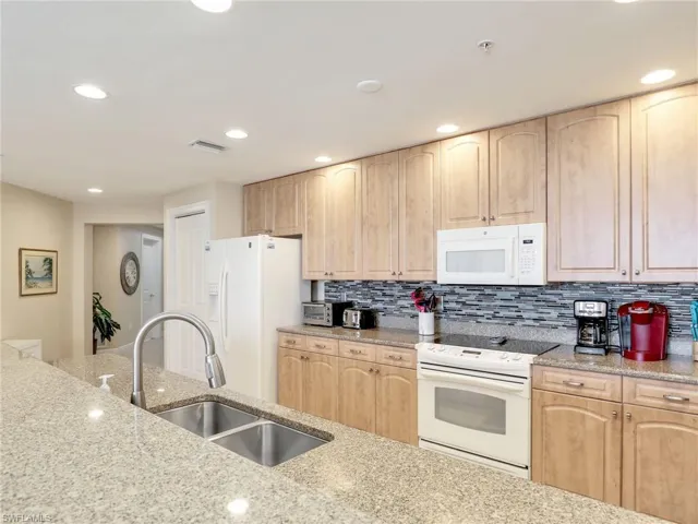 Kitchen with light stone countertops, white appliances, light brown cabinetry, backsplash, and sink