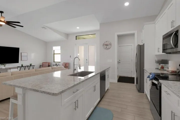 Kitchen island with light-toned countertop and integrated sink, white cabinetry with silver-toned hardware, stainless steel appliances, and wood-finish flooring