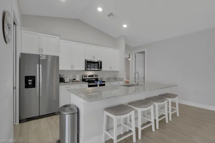 Vaulted ceiling, recessed lighting, white cabinetry, stainless steel appliances, and a kitchen island with stone countertop