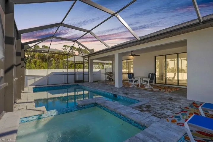 Screened-in outdoor living space featuring a swimming pool, spa, and covered patio with ceiling fan