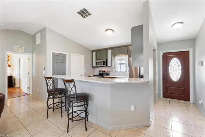 Kitchen featuring light wood-type flooring, light stone counters, vaulted ceiling, appliances with stainless steel finishes, and a kitchen breakfast bar