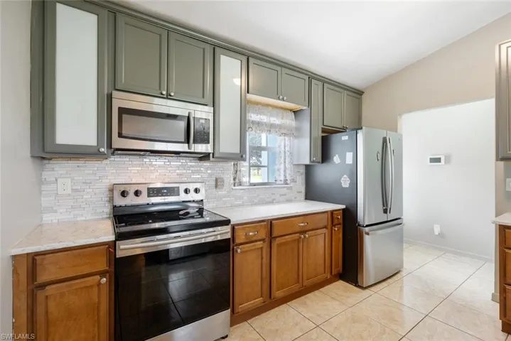 Kitchen with light tile patterned floors, backsplash, light stone counters, stainless steel appliances, and vaulted ceiling