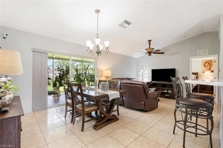 Dining space featuring light tile patterned flooring, ceiling fan with notable chandelier, and vaulted ceiling
