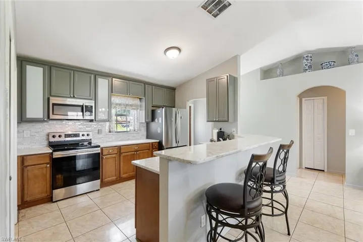 Kitchen with stainless steel appliances, light stone counters, vaulted ceiling, light tile patterned floors, and a kitchen breakfast bar