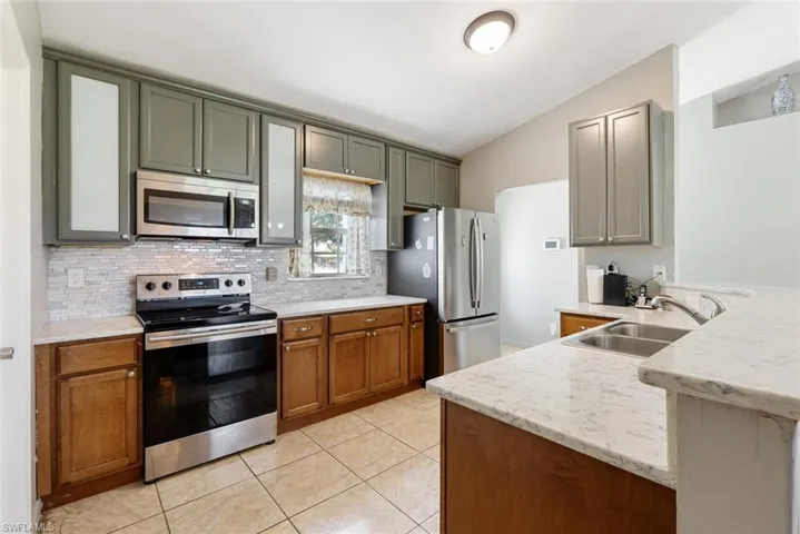 Kitchen with light tile patterned flooring, lofted ceiling, backsplash, stainless steel appliances, and sink