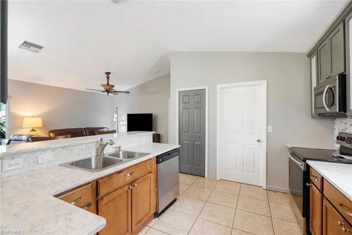 Kitchen featuring appliances with stainless steel finishes, sink, lofted ceiling, light tile patterned flooring, and ceiling fan
