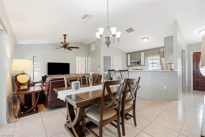 Dining area with light tile patterned flooring, ceiling fan with notable chandelier, and vaulted ceiling