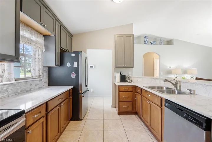 Kitchen featuring gray cabinets, stainless steel appliances, sink, vaulted ceiling, and light tile patterned floors