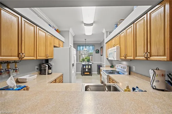 Kitchen with sink, crown molding, pendant lighting, white appliances, and light tile patterned flooring
