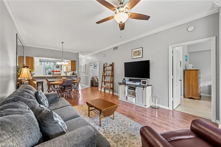Living room with ceiling fan with notable chandelier, crown molding, and light hardwood / wood-style flooring