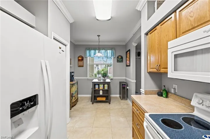 Kitchen with decorative light fixtures, white appliances, sink, and ornamental molding