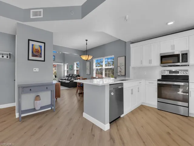 Kitchen featuring stainless steel appliances, decorative light fixtures, white cabinetry, a peninsula, and light stone counters