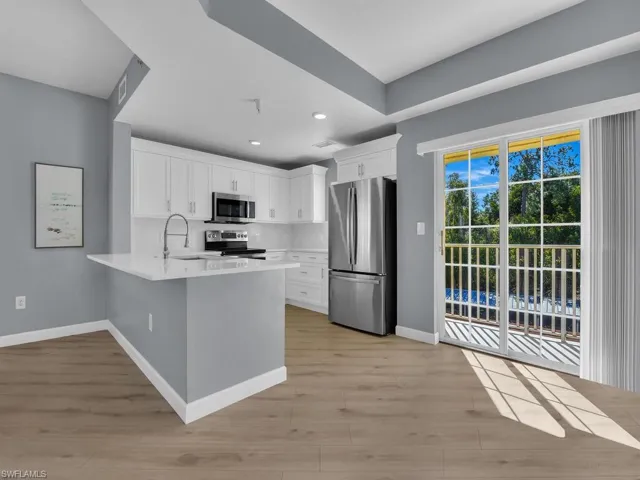 Kitchen featuring stainless steel appliances, white cabinets, a peninsula, light wood-style floors, and light stone counters