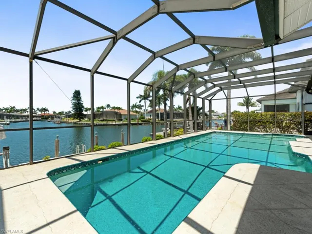 Outdoor pool with a water view, glass enclosure, and a patio area