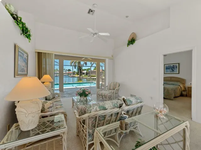 Carpeted living room featuring a water view, a ceiling fan, visible vents, high vaulted ceiling, and a sunroom