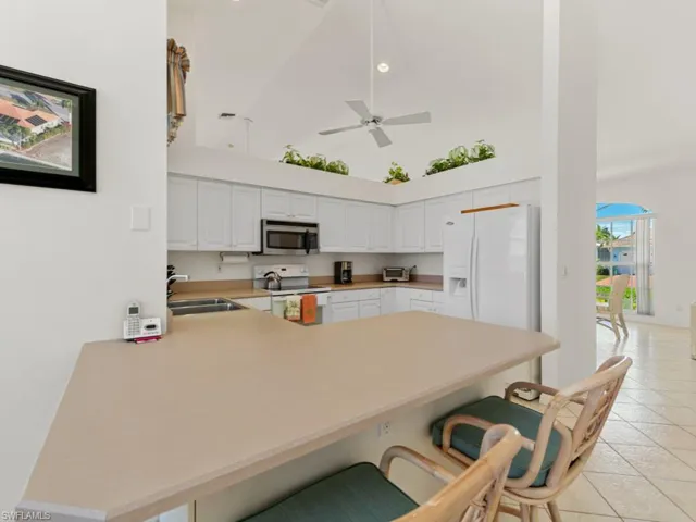 Kitchen with a kitchen breakfast bar, white appliances, light tile patterned floors, a peninsula, and a sink