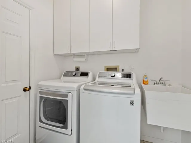 Clothes washing area featuring a sink, washer and clothes dryer, and cabinet space