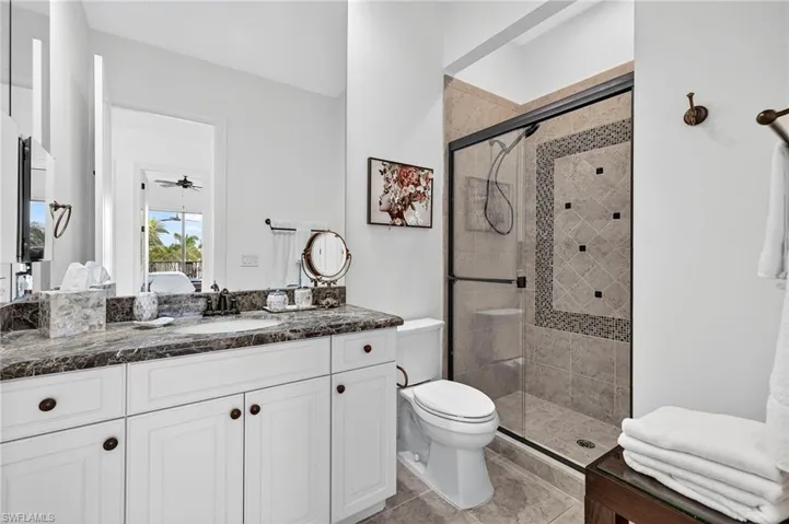 Ensuite bathroom featuring vanity, a stall shower, ceiling fan, and light tile patterned floors