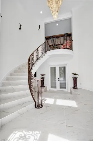 Staircase with french doors, a chandelier, marble finish flooring, recessed lighting, and ornamental molding