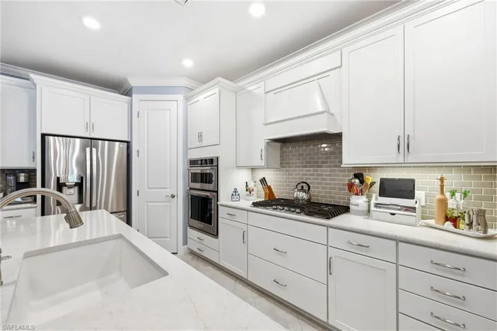 Kitchen featuring white cabinets, stainless steel appliances, ornamental molding, recessed lighting, and light stone countertops