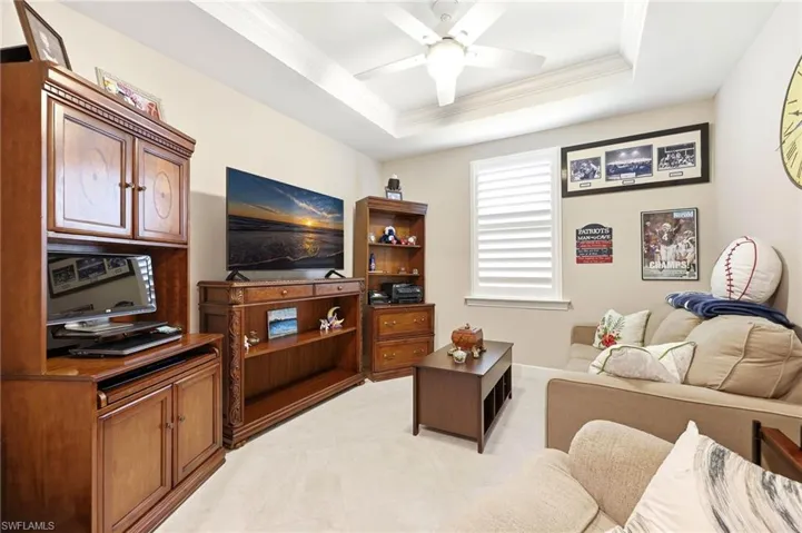 Living room with crown molding, a ceiling fan, and a raised ceiling