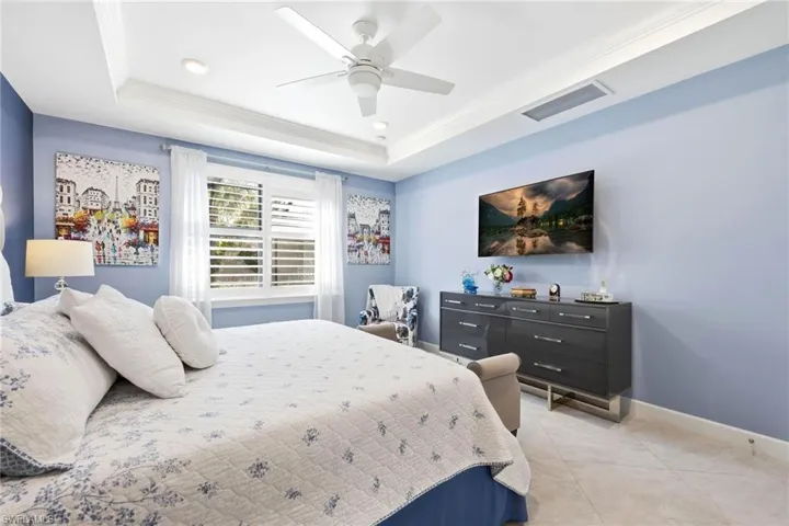 Bedroom with crown molding, recessed lighting, ceiling fan, light tile patterned flooring, and a tray ceiling
