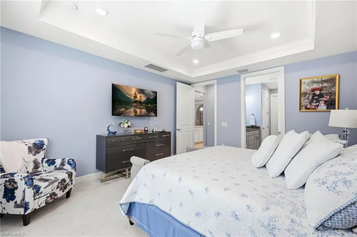 Bedroom featuring a raised ceiling, recessed lighting, ornamental molding, ceiling fan, and ensuite bathroom
