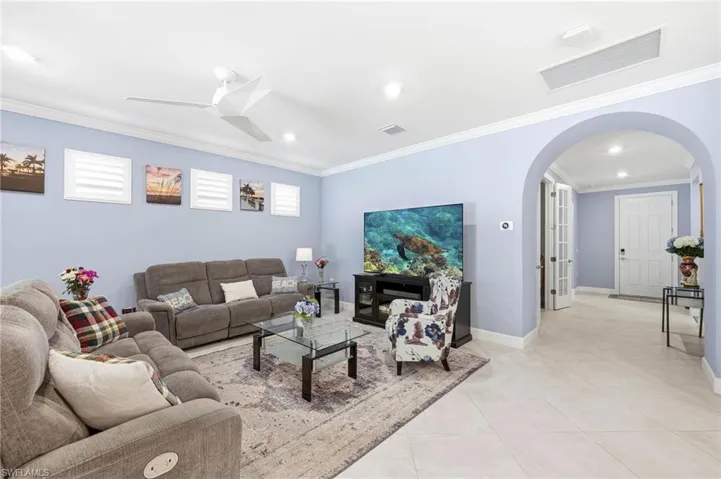 Living room with arched walkways, ornamental molding, ceiling fan, light tile patterned floors, and recessed lighting