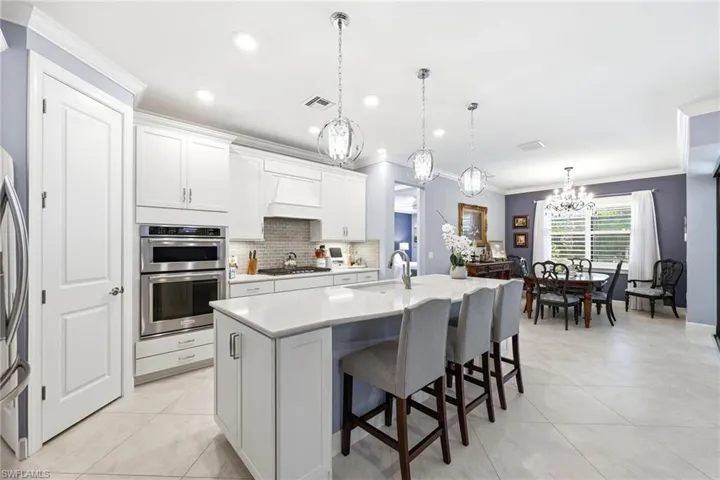 Kitchen with white cabinets, a kitchen breakfast bar, ornamental molding, a chandelier, and an island with sink