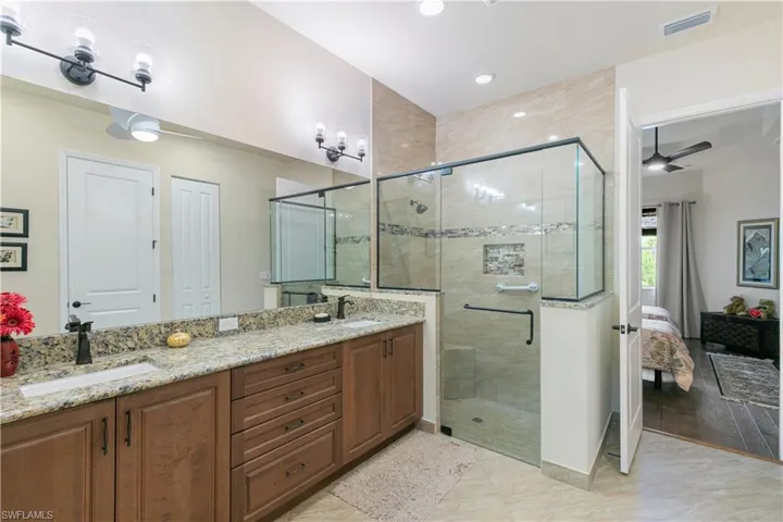 Ensuite bathroom featuring a stall shower, double vanity, and ceiling fan