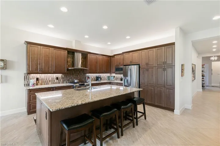 Kitchen featuring wall chimney exhaust hood, appliances with stainless steel finishes, an island with sink, decorative backsplash, and recessed lighting