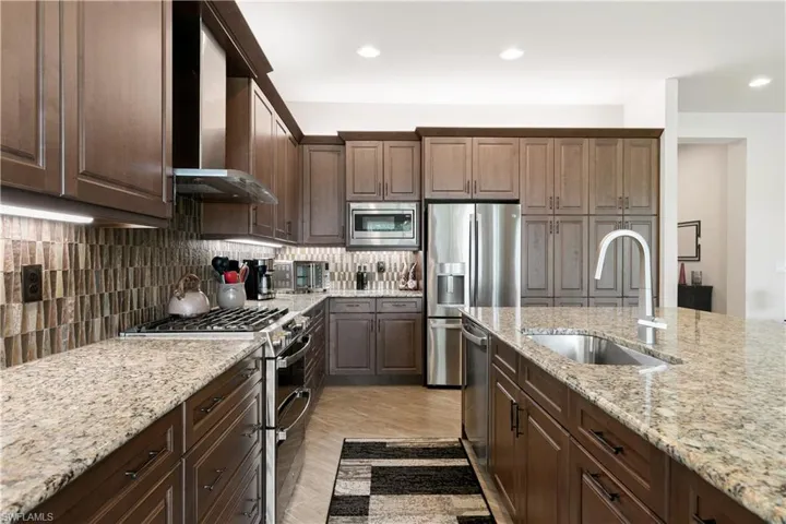 Kitchen featuring appliances with stainless steel finishes, a sink, wall chimney range hood, tasteful backsplash, and recessed lighting