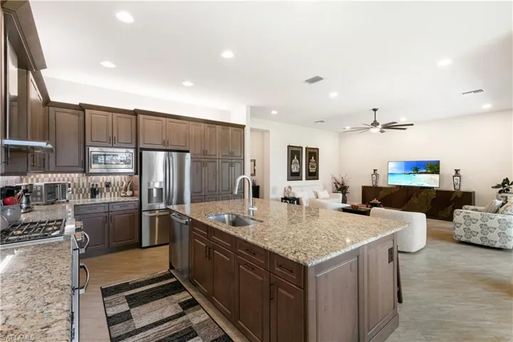 Kitchen featuring appliances with stainless steel finishes, a sink, backsplash, a ceiling fan, and a kitchen island with sink