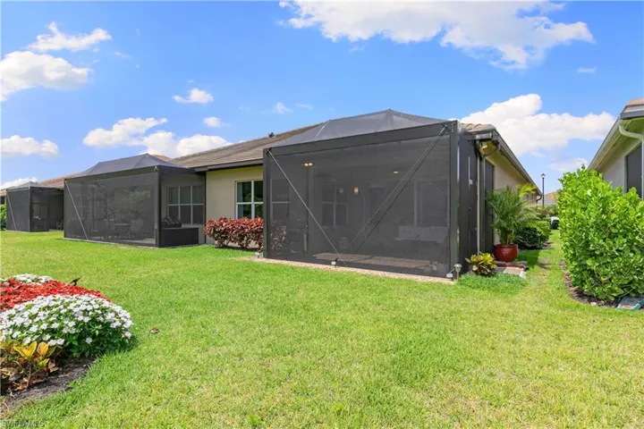 Rear view of property featuring a yard, glass enclosure, and stucco siding