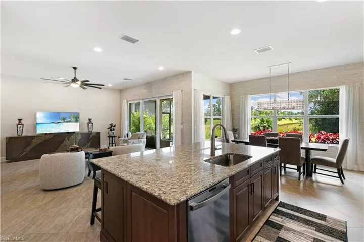 Kitchen with a sink, stainless steel dishwasher, a center island with sink, light stone countertops, and dark brown cabinets