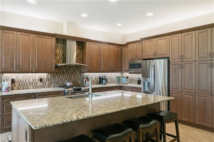 Kitchen featuring wall chimney range hood, a sink, appliances with stainless steel finishes, a breakfast bar area, and backsplash