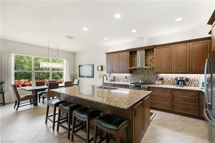 Kitchen featuring wall chimney range hood, a sink, stainless steel appliances, tasteful backsplash, and recessed lighting