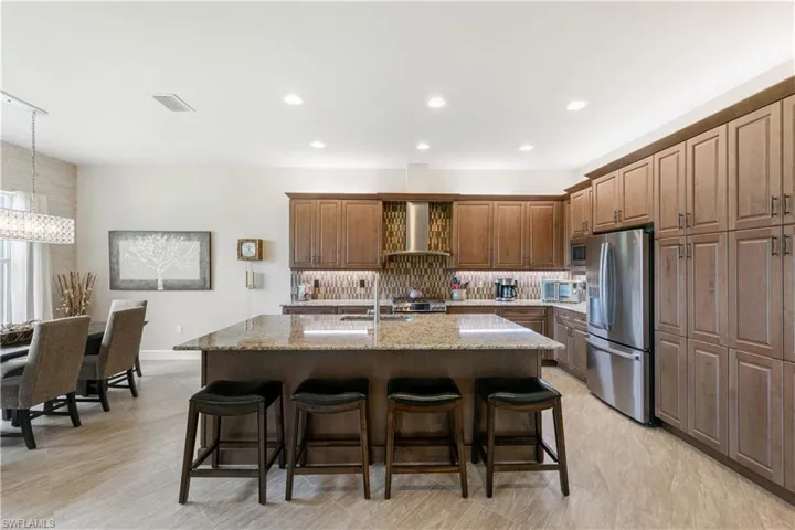 Kitchen featuring stainless steel fridge, wall chimney exhaust hood, tasteful backsplash, a breakfast bar area, and a kitchen island with sink