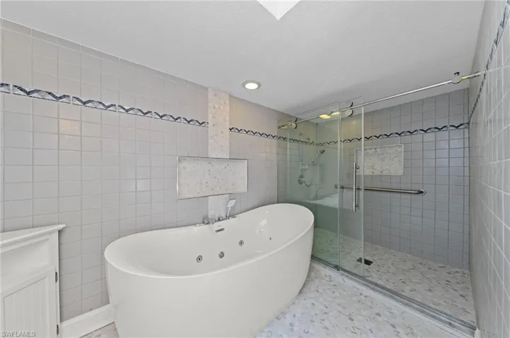 Bathroom with tile walls, a freestanding bath, a shower stall, and recessed lighting
