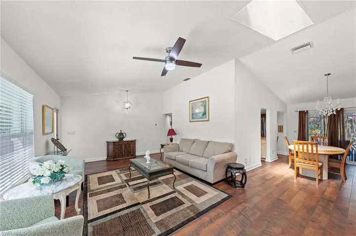 Living area featuring a chandelier, a skylight, dark wood-type flooring, a ceiling fan, and lofted ceiling